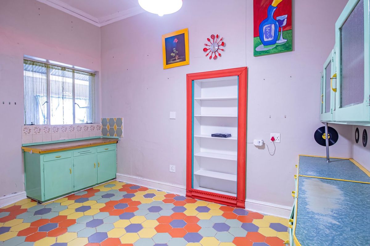 A retro-style kitchen featuring vintage mint green cabinetry, colorful hexagonal floor tiles, and a built-in recessed shelving unit with a vibrant red frame.