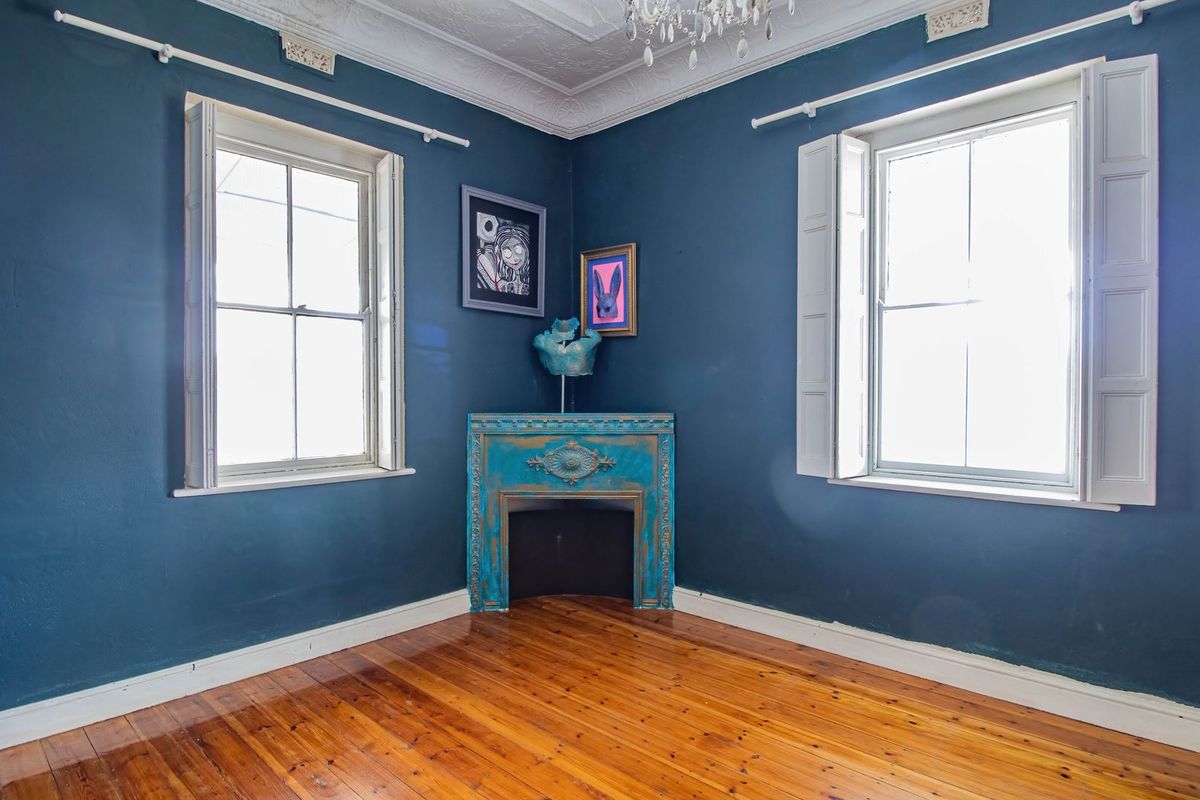 A bedroom featuring polished timber flooring, ornate ceiling cornices, and a decorative corner fireplace mantel.