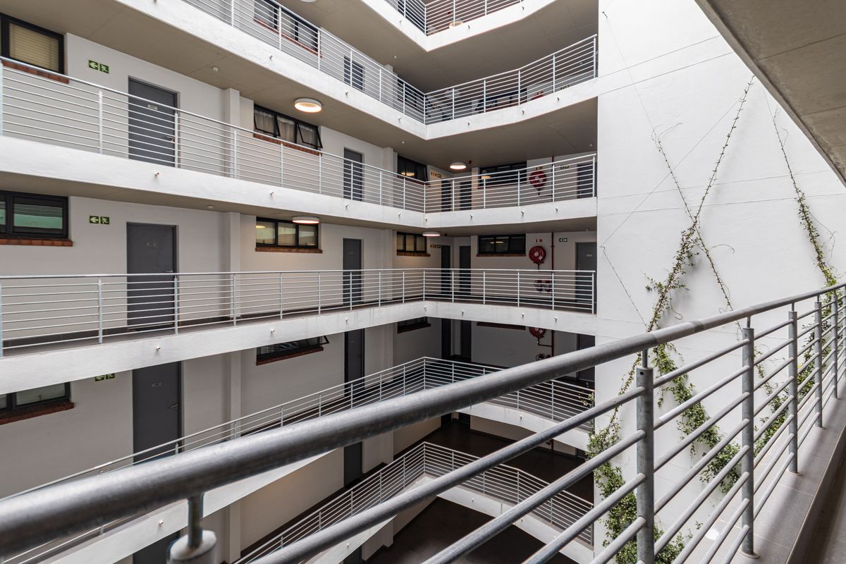 View of the apartment building's central atrium featuring multi-level walkways with metal railings and access doors to individual units.