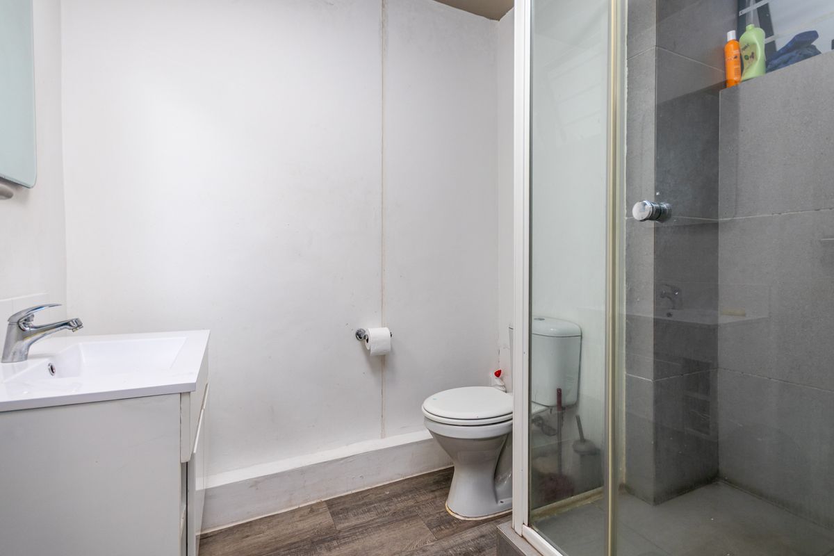 A functional bathroom featuring a vanity basin, a standard toilet, and a glass-enclosed shower with grey tiled walls and wood-look flooring.