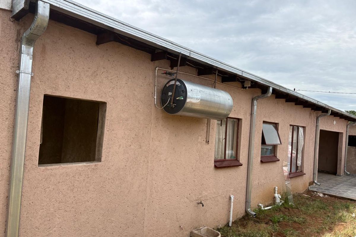 Rear exterior view of the property featuring a wall-mounted geyser, exposed plumbing, and unfinished window openings.