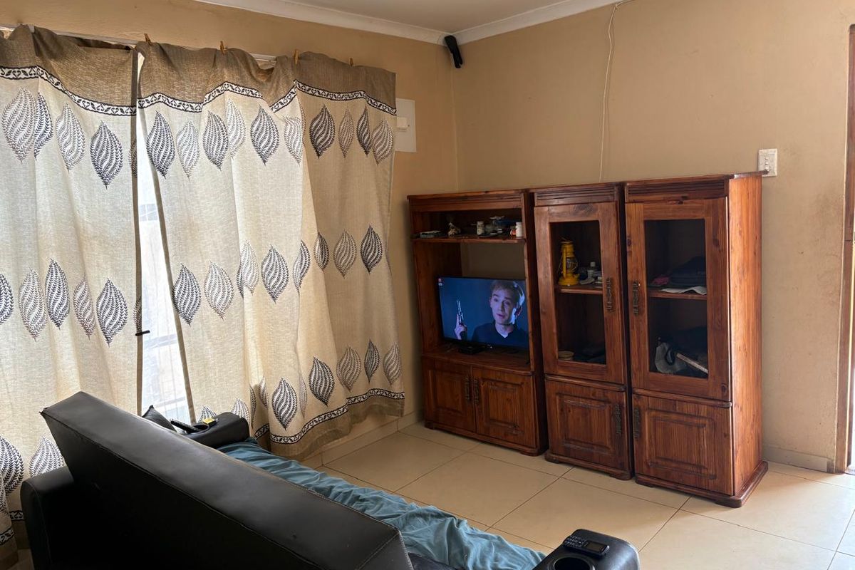 A living room featuring tiled flooring and large sliding glass doors with curtains, providing access to the exterior.