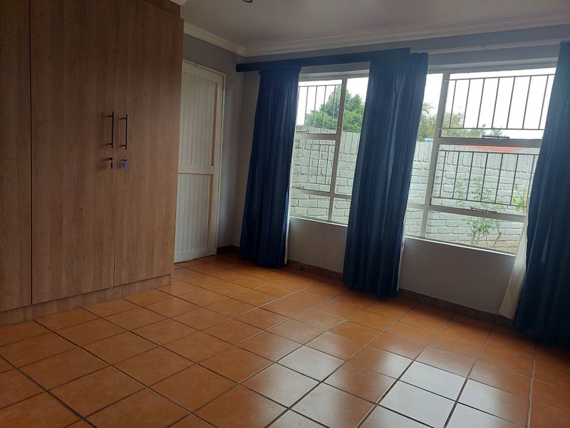 A bright, empty bedroom featuring tiled flooring, a built-in wardrobe, and windows fitted with security bars.