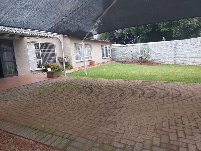 A covered patio area featuring a shade sail, paved flooring, and access to a private garden with a brick boundary wall.