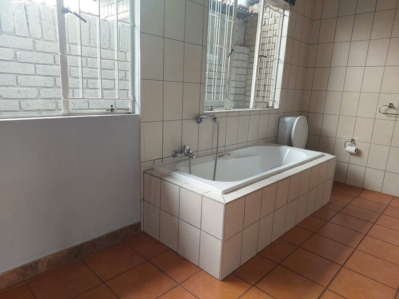 A functional bathroom featuring a built-in tiled bathtub, ceramic floor tiles, and security bars on the windows.