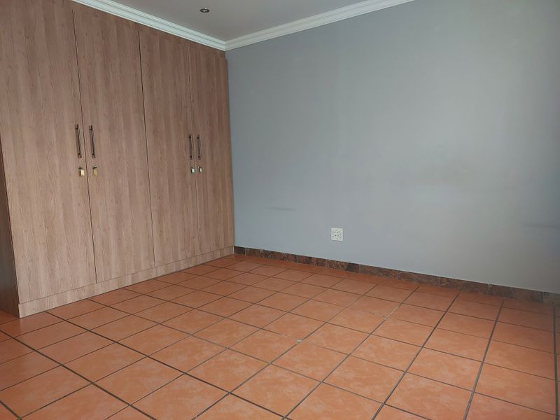 An empty bedroom featuring built-in wooden cupboards, tiled flooring, and neutral grey walls, offering a clean and versatile space ready for personalization.