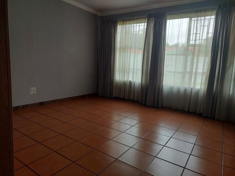 An empty bedroom featuring terracotta-style floor tiles, neutral grey walls, and large windows fitted with curtain rails and sheer curtains.