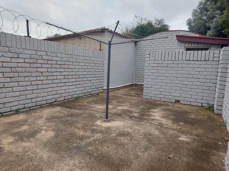A private rear courtyard area featuring painted brick boundary walls with security razor wire and concrete paving.