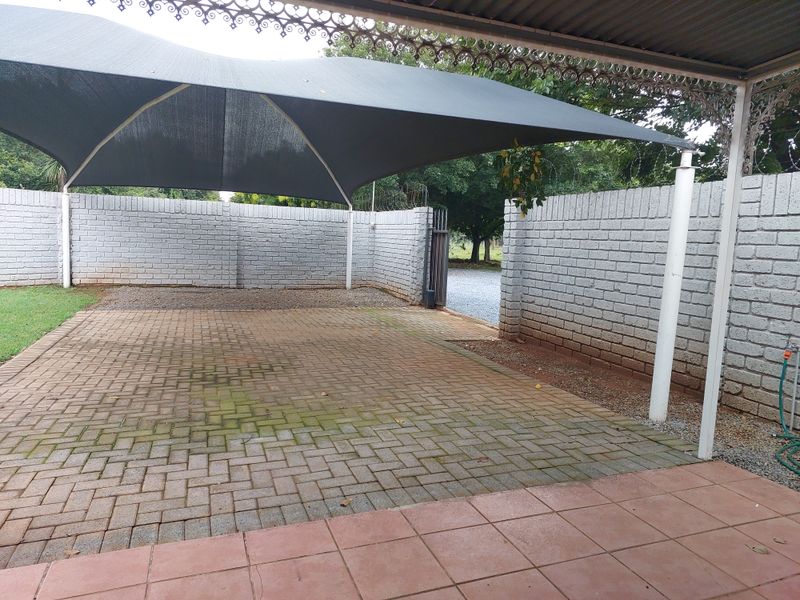 A covered outdoor patio area featuring paved flooring, a shade sail structure, and enclosed by brick boundary walls with a gated entrance.
