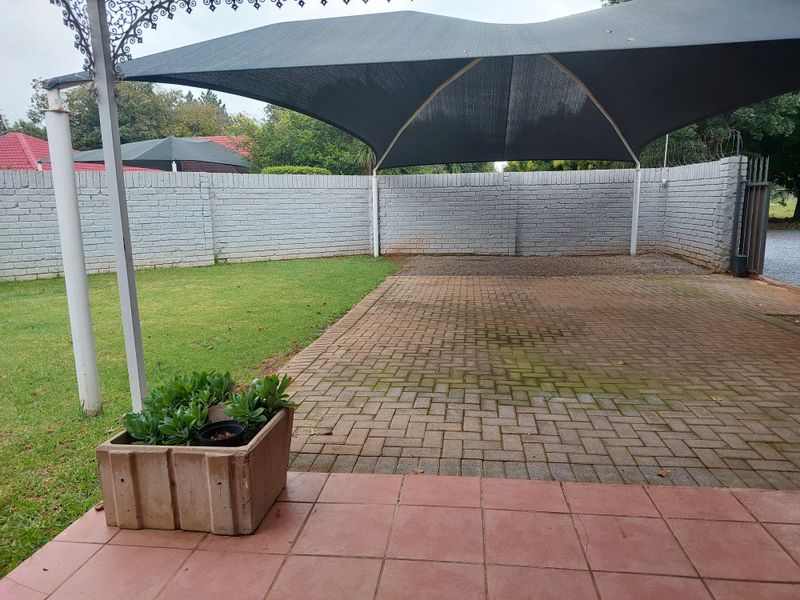 Outdoor paved patio area featuring a shade sail structure and enclosed by a brick boundary wall.