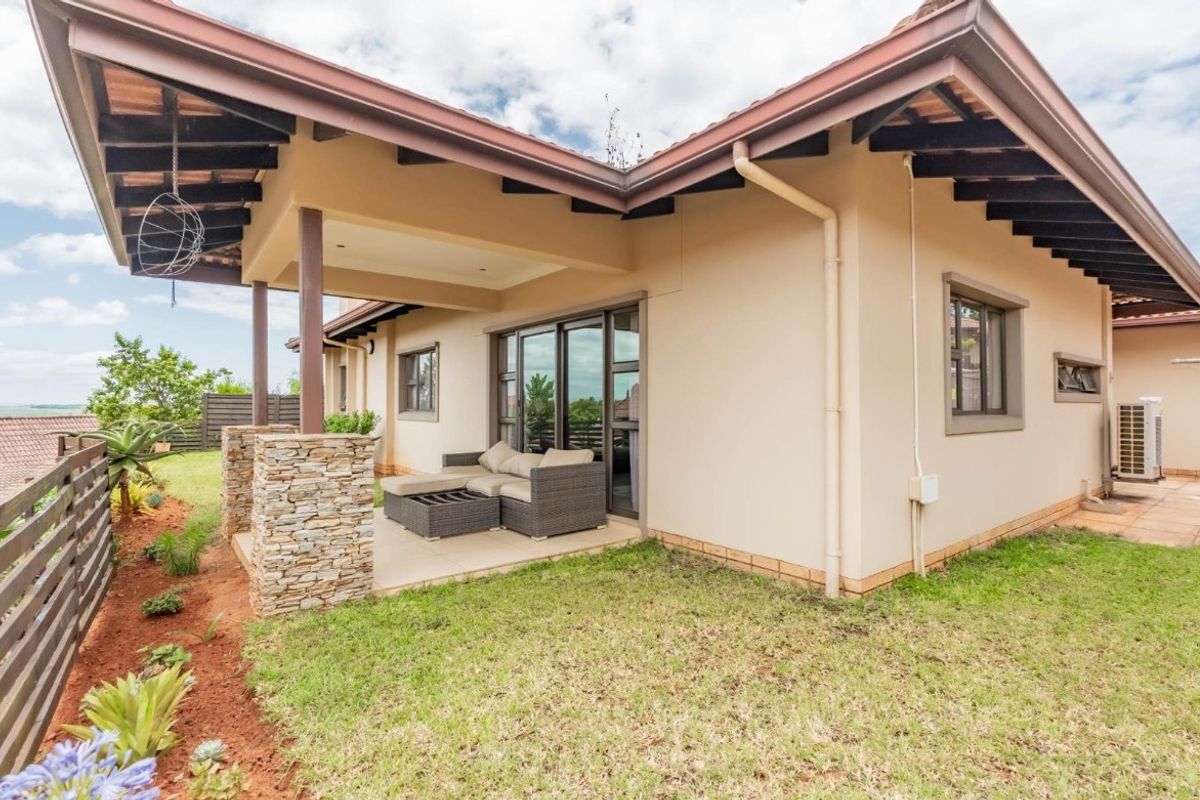 Rear view of the house featuring a covered patio with stone-clad pillars, exposed timber rafters, and sliding glass doors leading to the garden.