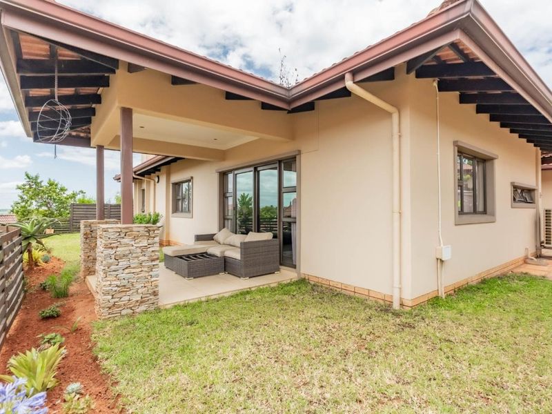 Rear view of the house featuring a covered patio with stone-clad pillars, exposed timber rafters, and sliding glass doors leading to the garden.