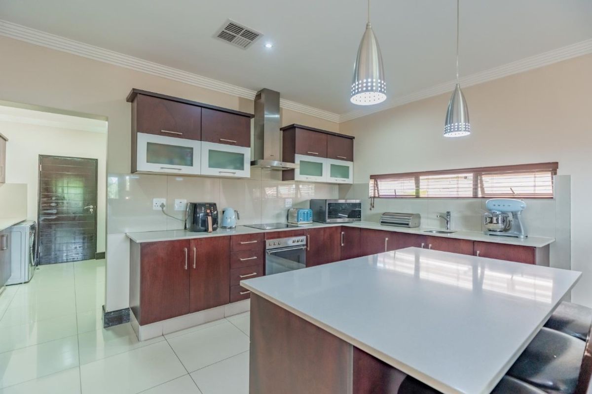 Modern kitchen featuring dark wood cabinetry, stone countertops, a central island, and integrated stainless steel appliances, complemented by tiled flooring and pendant lighting.