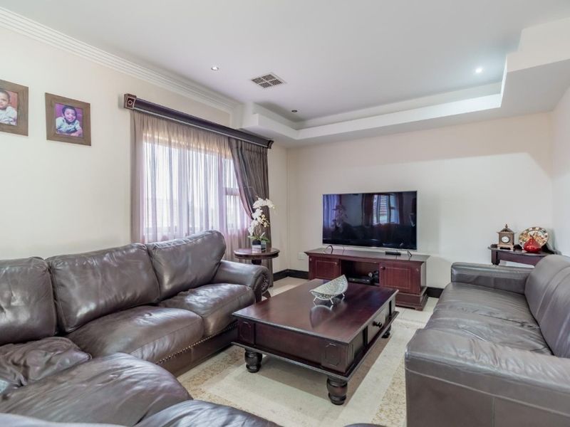 A well-maintained living room featuring a recessed ceiling with downlights, ducted air conditioning, and neutral tiled flooring.