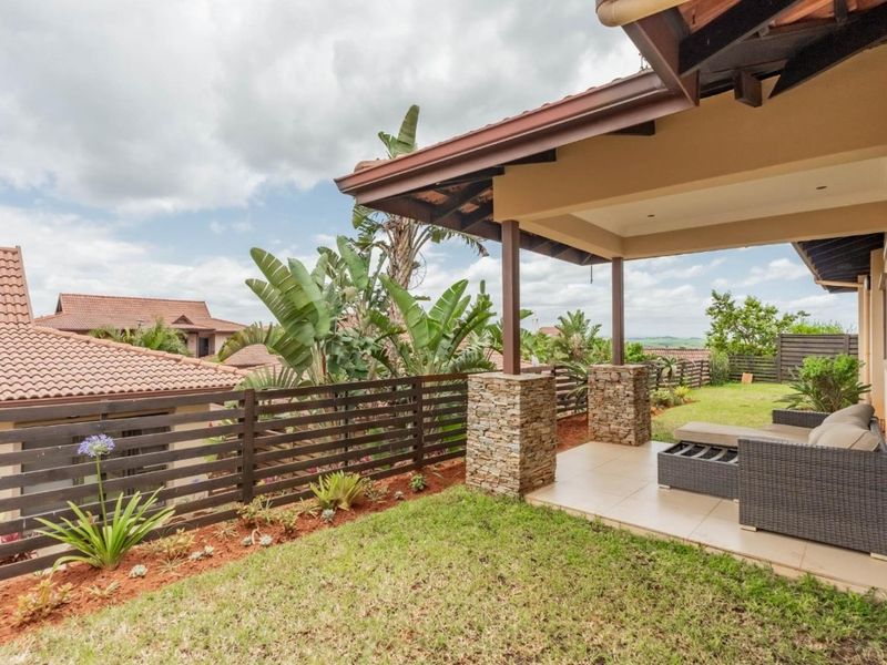 A covered patio area featuring stone-clad columns and tiled flooring, overlooking a landscaped garden with timber-style fencing.