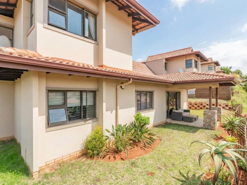 Rear view of the double-storey house featuring a covered patio, stone-clad pillars, terracotta roof tiles, and a well-maintained garden area.