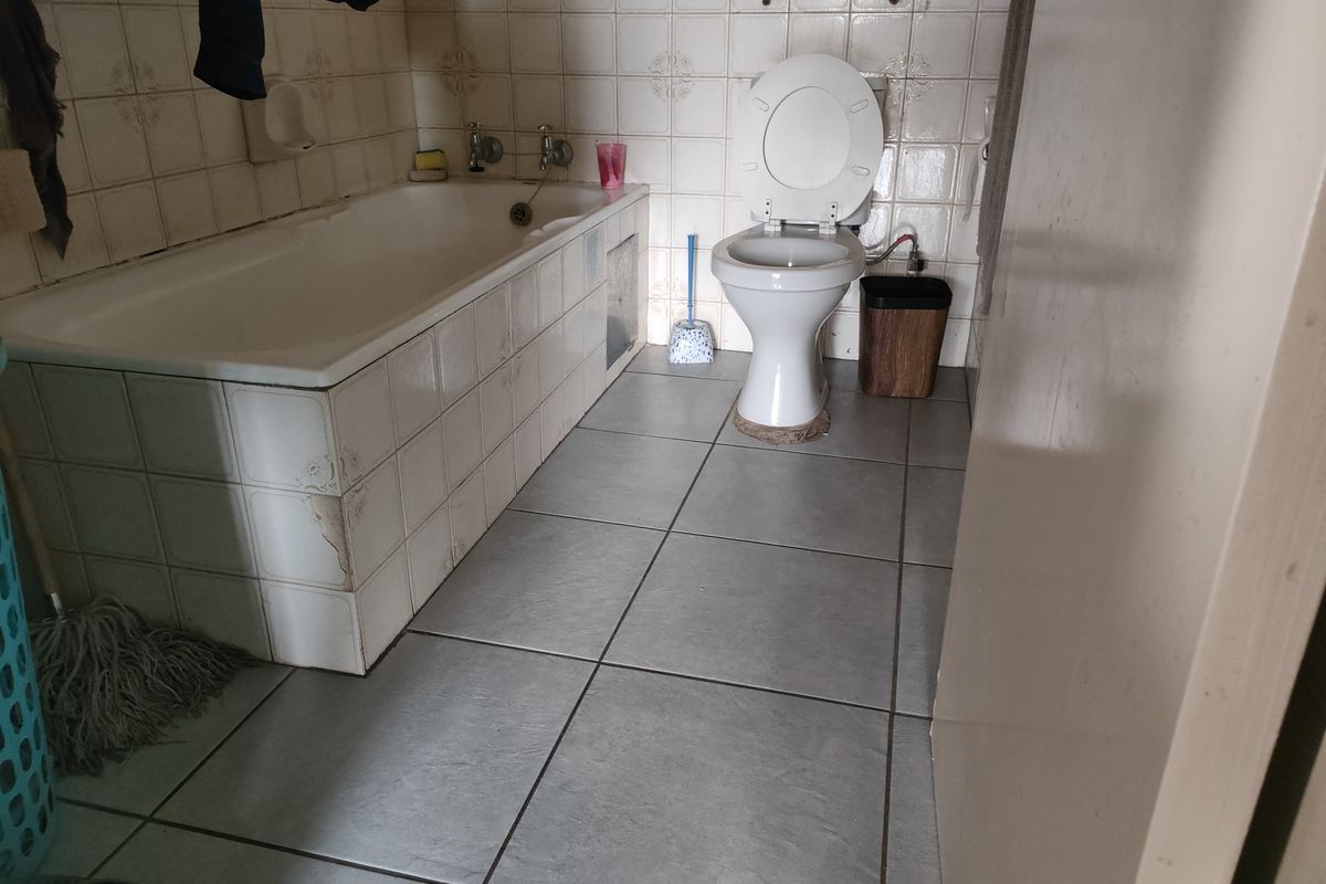 A dated bathroom featuring a built-in bathtub with tiled surround and a standard toilet, requiring cosmetic updates to modernize the space.