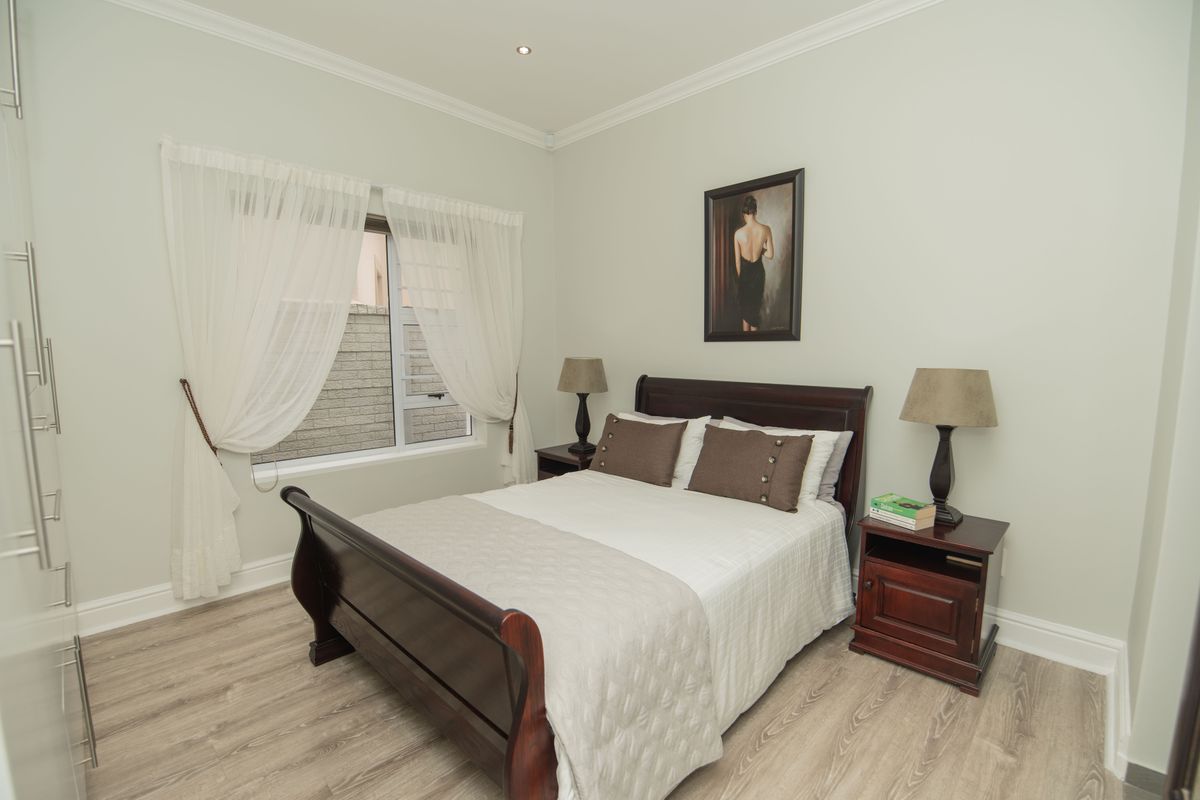 A well-maintained bedroom featuring light-toned wood-look flooring, built-in cupboards, and neutral wall finishes.