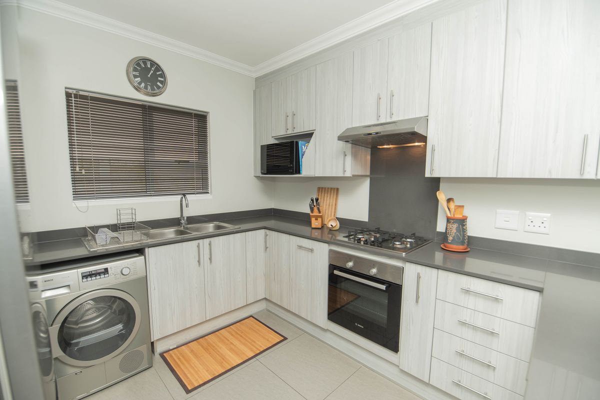 Modern kitchen featuring light wood-grain cabinetry, dark stone countertops, built-in oven, gas hob, extractor fan, and integrated laundry appliance space.