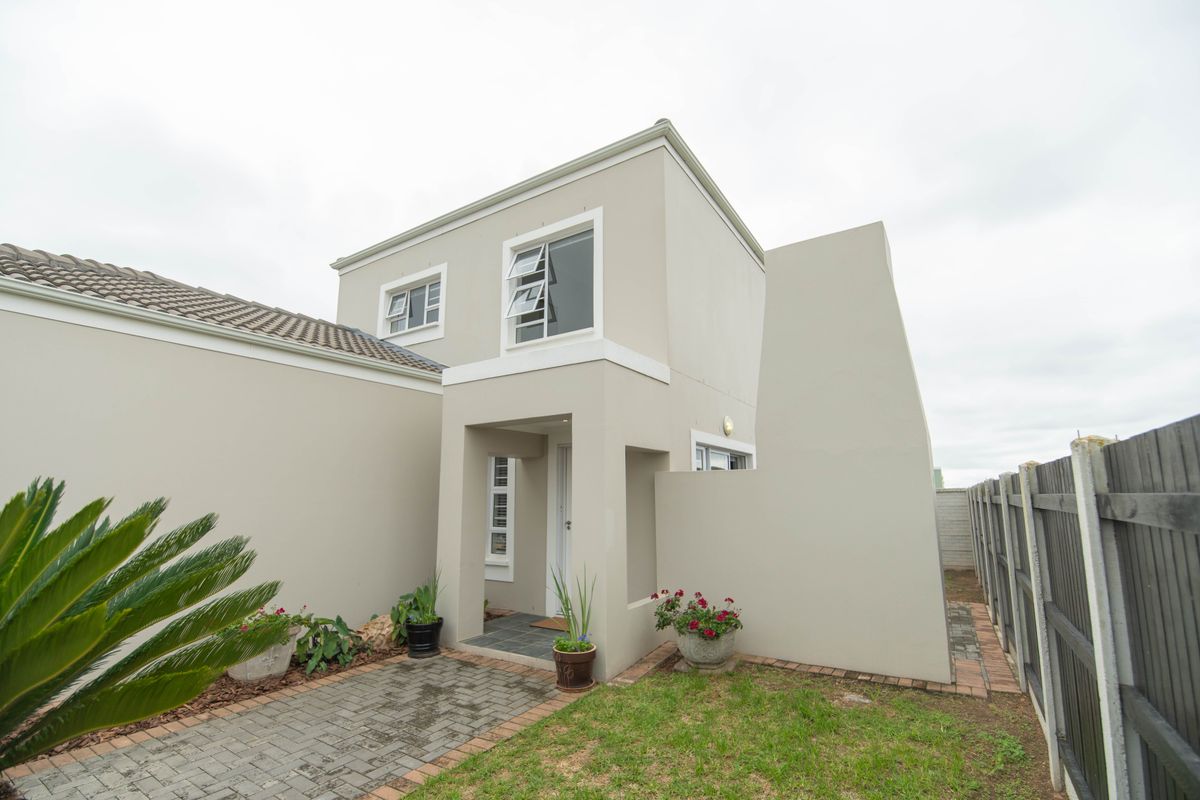 A modern two-story residential exterior featuring a paved walkway, small garden area, and neutral-toned facade with aluminum window frames.