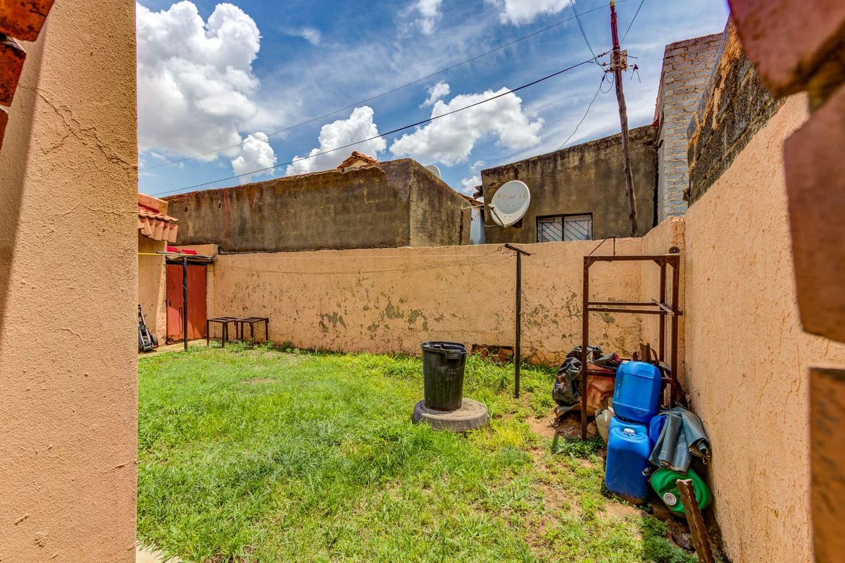 A private rear courtyard area featuring a small lawn, perimeter boundary walls, and a utility space for outdoor storage.