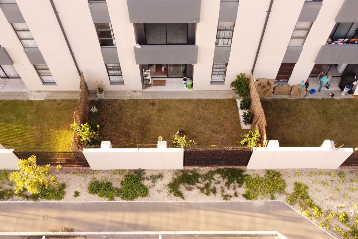 Aerial view of an apartment ground floor unit featuring a private garden area with perimeter fencing and direct access to the building exterior.