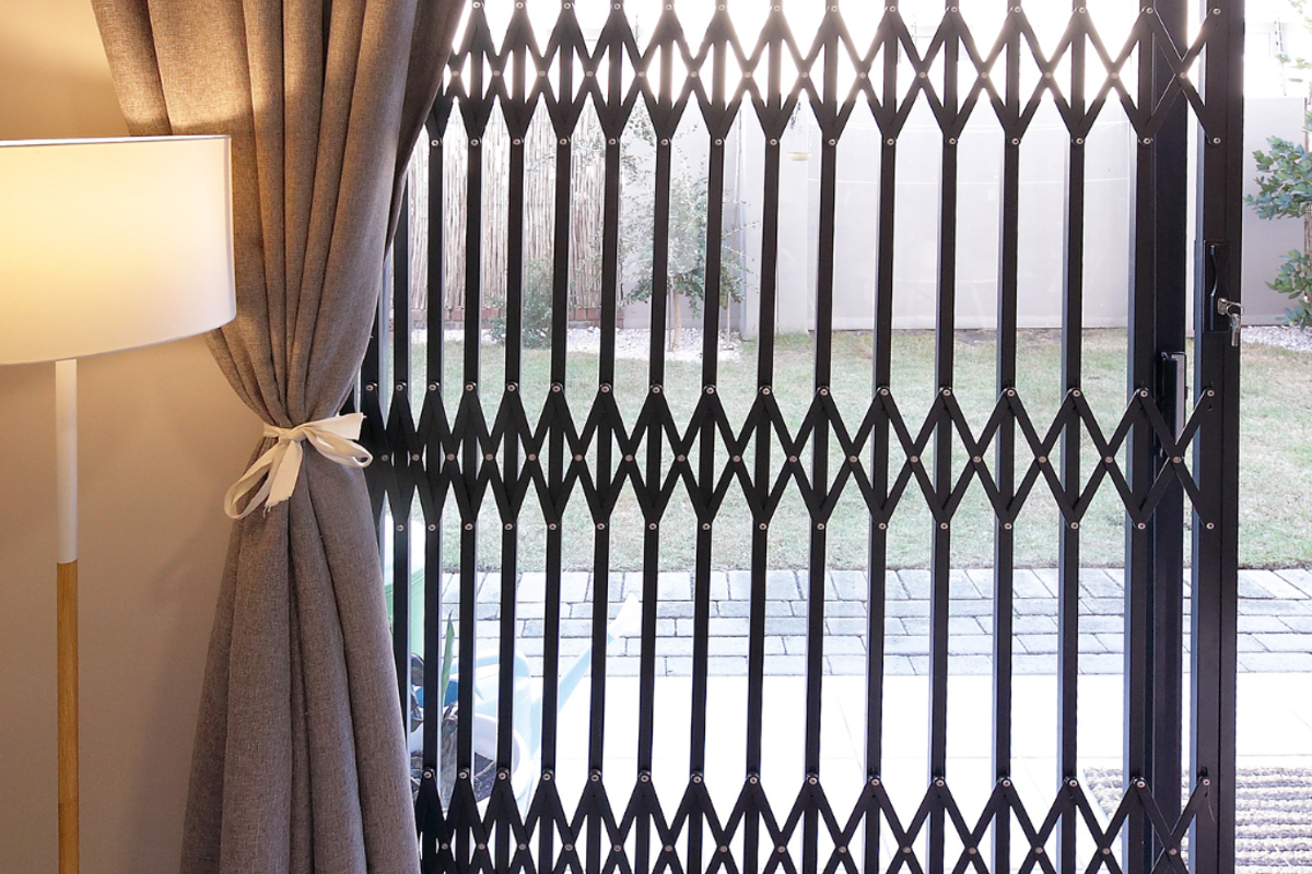 Interior view looking through a black security gate towards a paved patio and garden area.