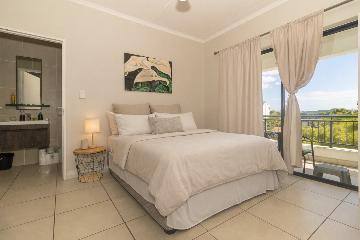 A bright bedroom featuring tiled flooring, an en-suite bathroom, and sliding glass doors leading to a private balcony with scenic views.