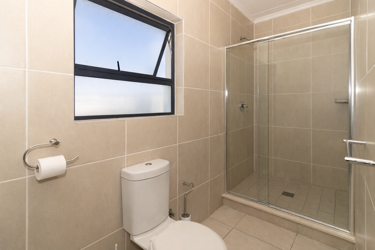 A clean, modern bathroom featuring neutral wall and floor tiles, a glass-enclosed shower, and a standard toilet.
