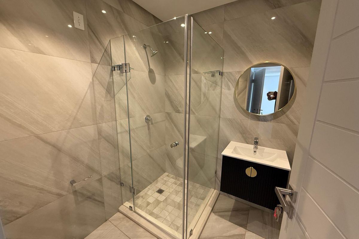 Modern bathroom featuring a glass-enclosed shower, wall-mounted vanity with basin, and contemporary large-format marble-look wall and floor tiling.