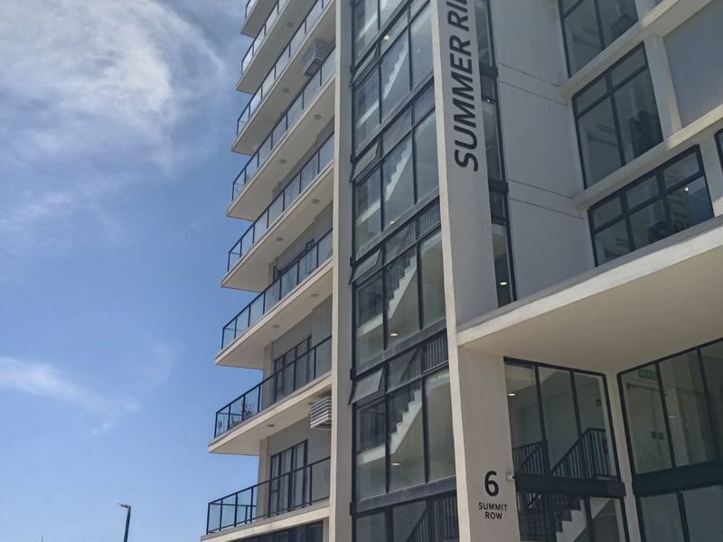Modern multi-story apartment building facade featuring glass balconies, large windows, and a prominent Summer Ridge signage.
