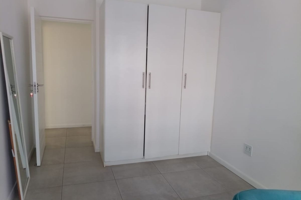 A bedroom featuring neutral floor tiles and a built-in white wardrobe, offering a clean and functional space.