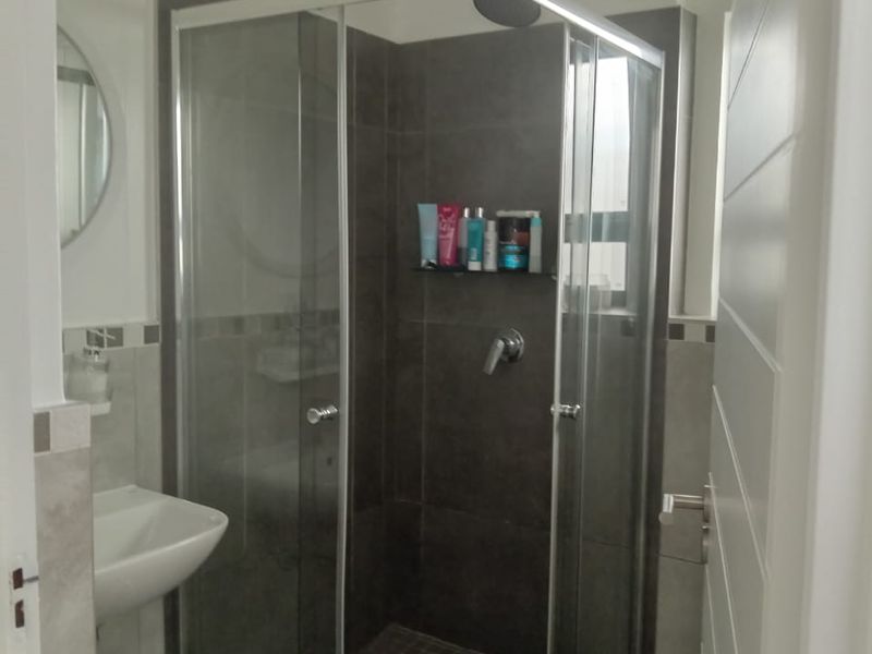 A modern bathroom featuring a glass-enclosed shower with dark tiled walls and a wall-mounted basin.