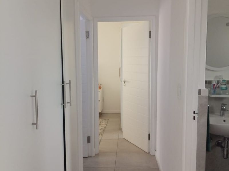 A bright hallway featuring neutral floor tiles and built-in storage cupboards, providing access to adjacent rooms including a bathroom.