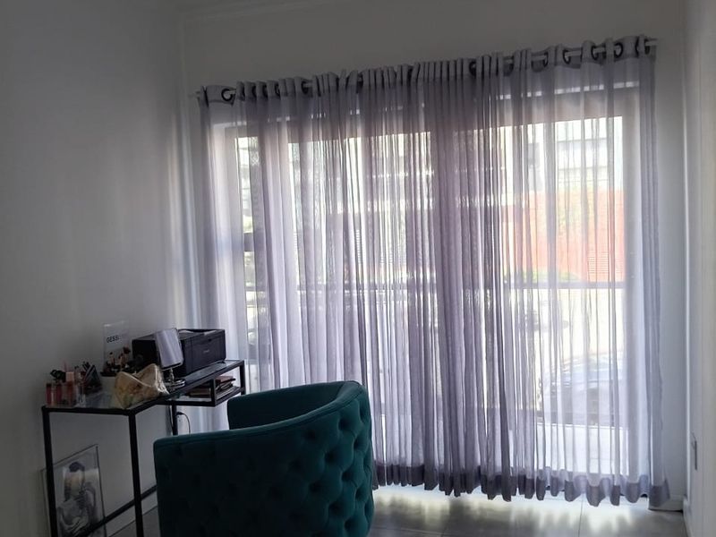 A bright living area featuring large sliding glass doors with sheer curtains, neutral floor tiles, and a clean, minimalist aesthetic.