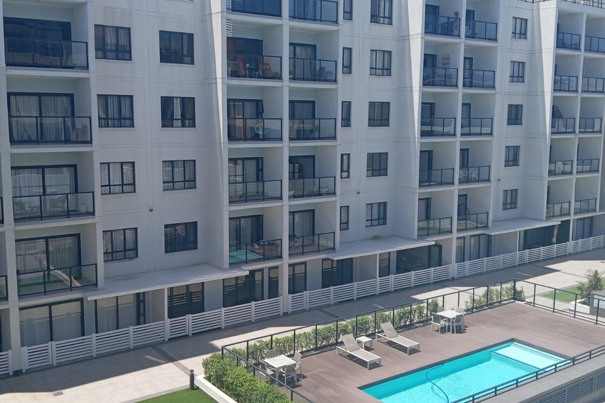 Elevated view of a modern apartment complex featuring a swimming pool, wooden deck, and landscaped lawn area.