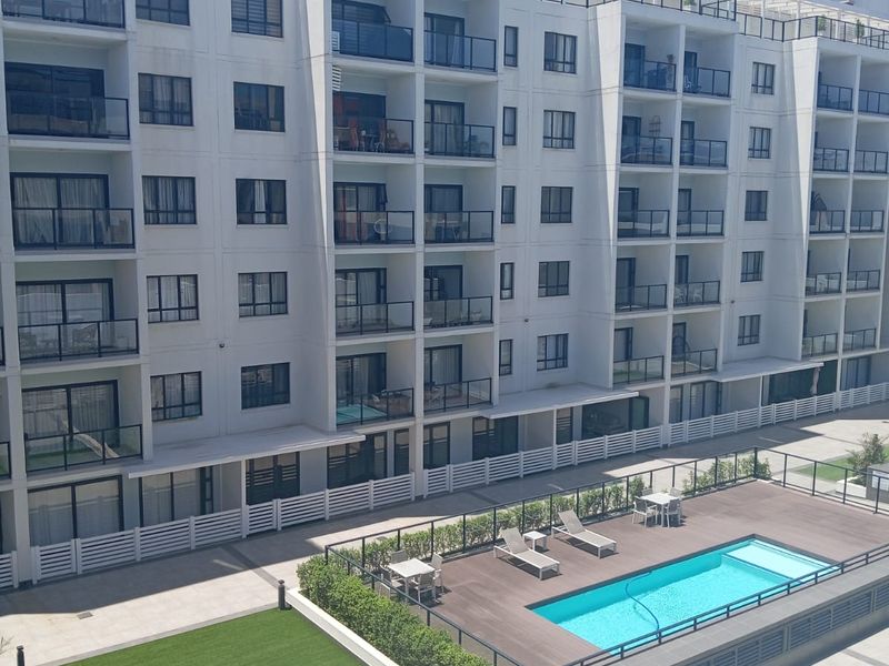 Elevated view of a modern apartment complex featuring a swimming pool, wooden deck, and landscaped lawn area.
