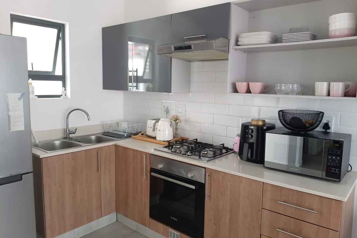 Modern kitchen featuring wood-look cabinetry, white subway tile backsplash, stone countertops, built-in oven, gas hob, and stainless steel extractor fan.