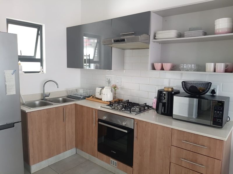 Modern kitchen featuring wood-look cabinetry, white subway tile backsplash, stone countertops, built-in oven, gas hob, and stainless steel extractor fan.