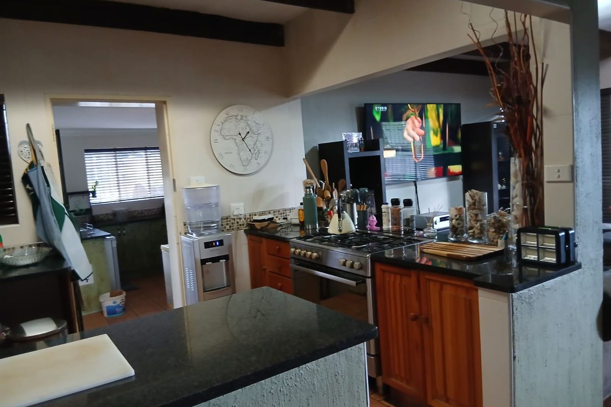 A functional kitchen featuring granite countertops, wooden cabinetry, a gas stove, and an adjacent scullery area with tiled flooring.