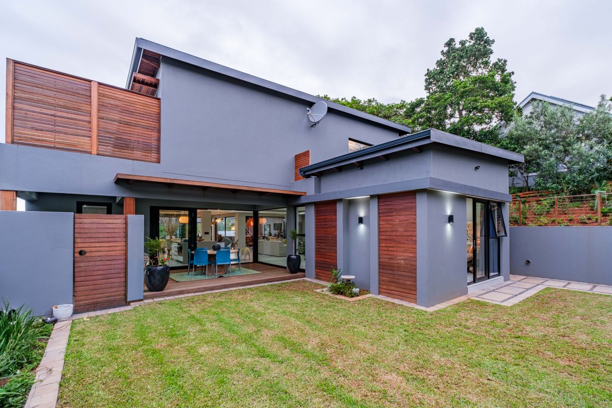 Modern rear exterior view featuring a landscaped garden, timber decking, and contemporary grey facade with wood panel accents.