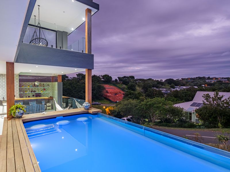 Modern elevated pool area featuring a timber deck, glass balustrades, and an integrated bar, offering expansive views of the surrounding landscape.