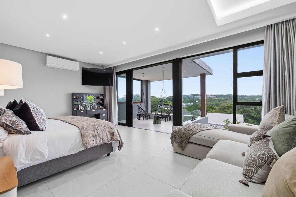 Spacious modern bedroom featuring large sliding glass doors that open onto a private balcony with scenic views and integrated air conditioning.