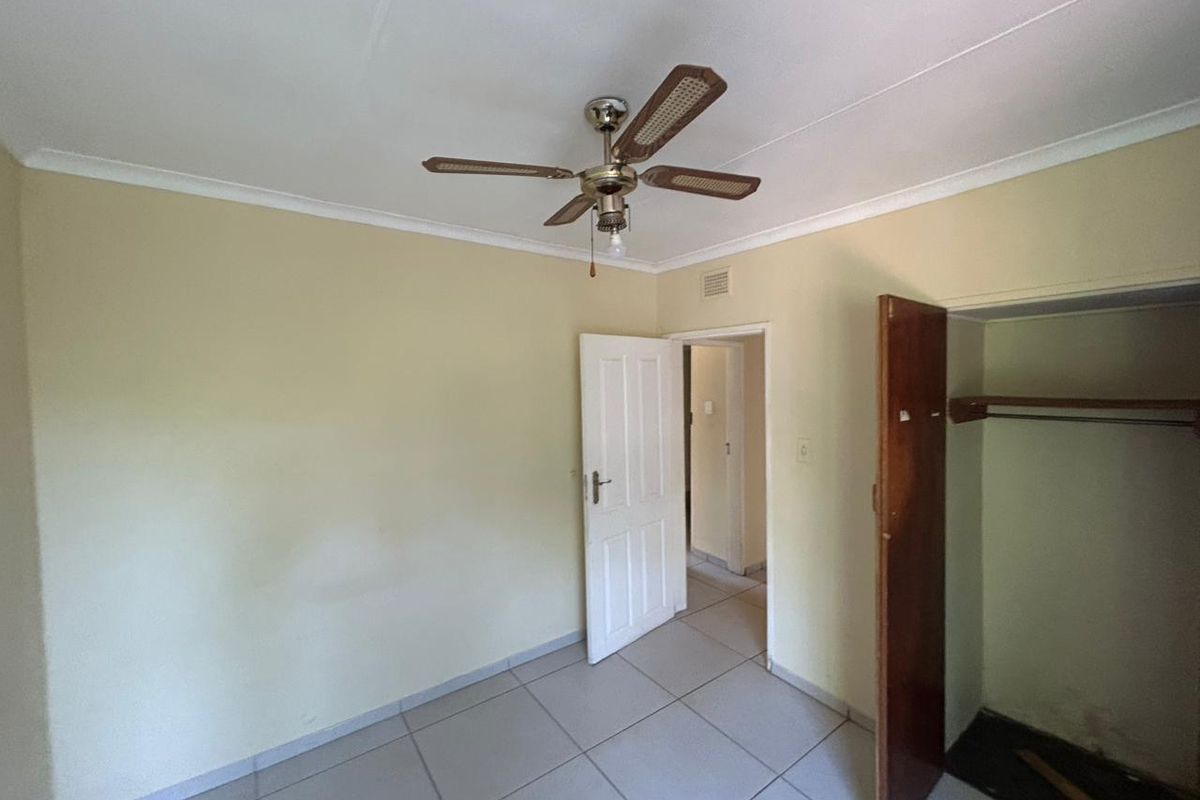 An empty bedroom featuring tiled flooring, a ceiling fan, and a built-in closet with wooden doors.