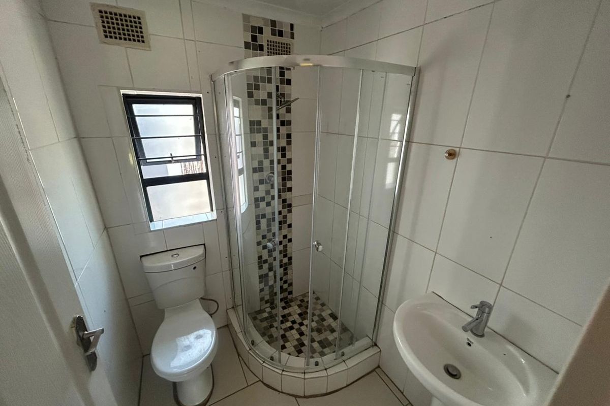 A functional bathroom featuring a corner shower enclosure with mosaic tile accents, a pedestal basin, and a standard toilet.