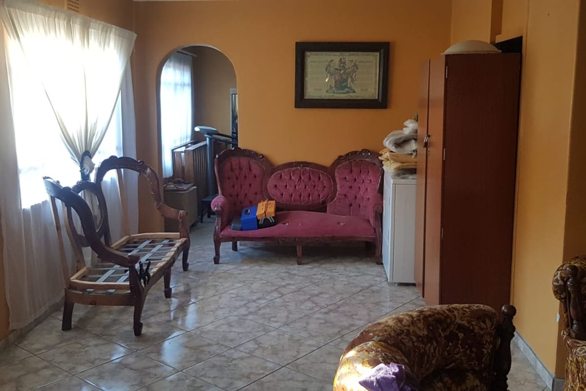 A living room featuring tiled flooring and an arched doorway leading to an adjacent space, with dated wall finishes.