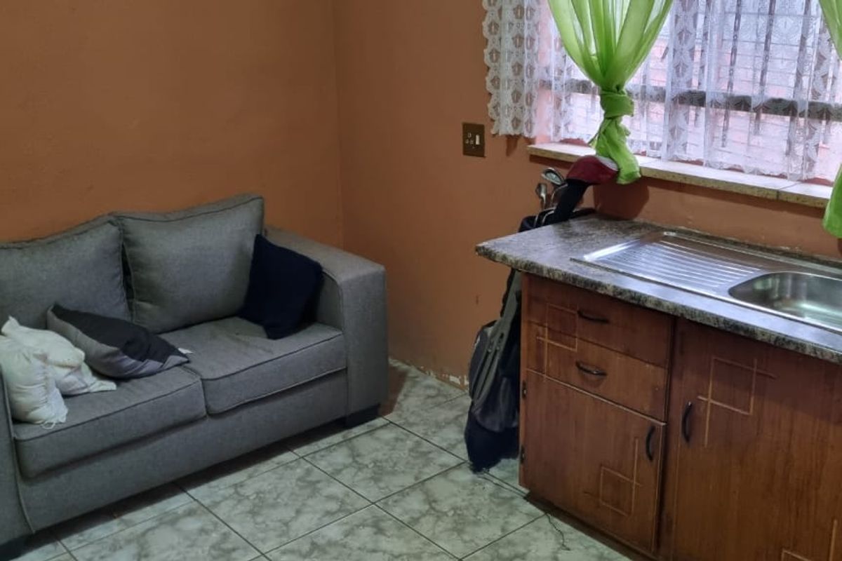 A functional kitchen area featuring built-in wooden cabinetry, a stainless steel sink, and tiled flooring, suitable for a compact living space.
