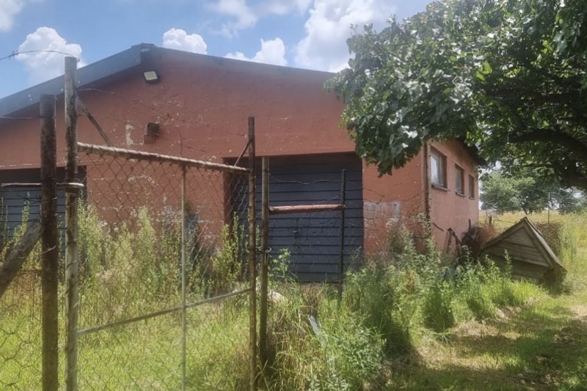 Exterior view of a farm outbuilding featuring a red masonry facade, garage doors, and surrounding chain-link fencing in need of maintenance.