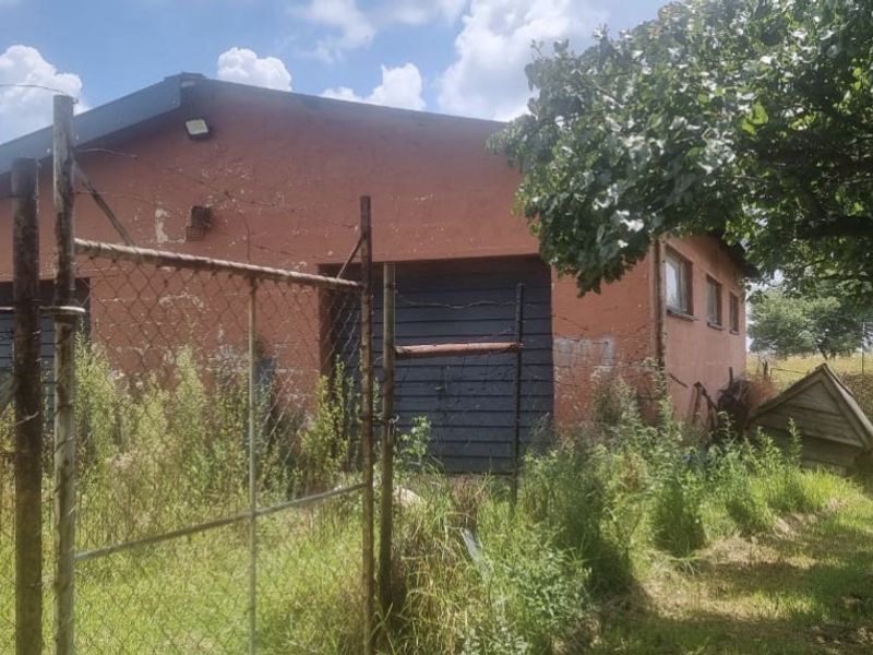 Exterior view of a farm outbuilding featuring a red masonry facade, garage doors, and surrounding chain-link fencing in need of maintenance.