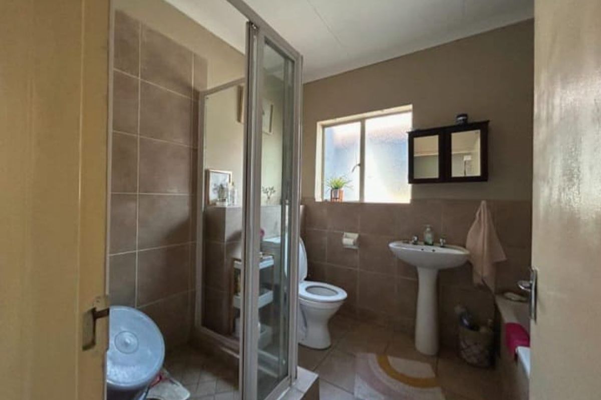 A functional bathroom featuring a pedestal sink, a glass-enclosed shower, and a toilet, finished with neutral wall tiles.